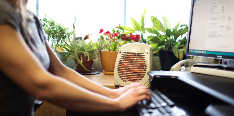 Woman using space heater at her desk in summer
