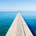 Endless wooden jetty over clean turquoise water to the horizon under blue clear summer sky. Noumea Beach, Noumea, New Caledonia, South West Pacific Ocean