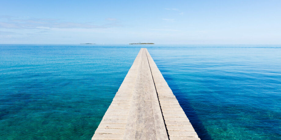 Endless wooden jetty over clean turquoise water to the horizon under blue clear summer sky. Noumea Beach, Noumea, New Caledonia, South West Pacific Ocean