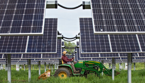 Byron Kominek, owner of Jack’s Solar Garden, tills the soil at the farm in Longmont, Colo. Photo shows Kominek on a tractor in between solar panels.