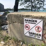 A sign attached to a concrete barrier reads “DANGER, NO SWIMMING’” and “DANGER, KEEP OFF ICE” in front of a private beach on the South Side of Chicago.