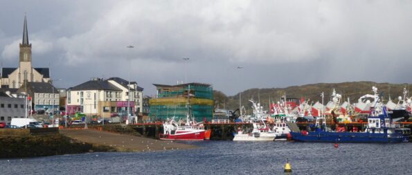 Image of Killybeg, Ireland port with fishing boats in the water and a town and hillside in the background. 